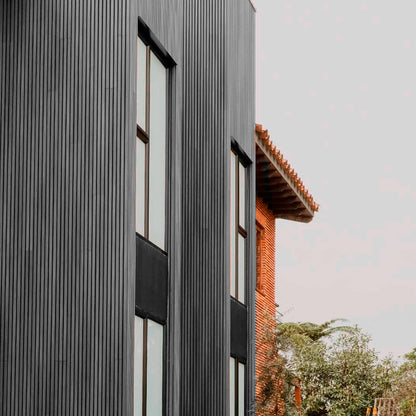 Revestimiento de fachada con cladding Wallpanel WPC gris instalado en muro exterior, terminación tipo madera en aplicación vertical
